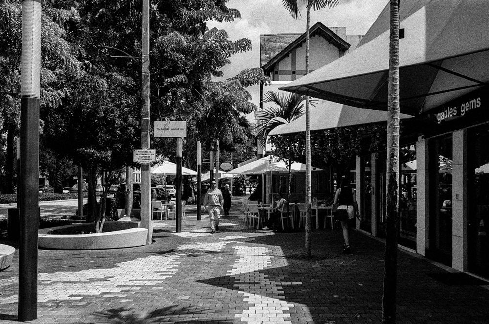 Black and white street scene with outdoor cafe umbrellas and storefronts.
