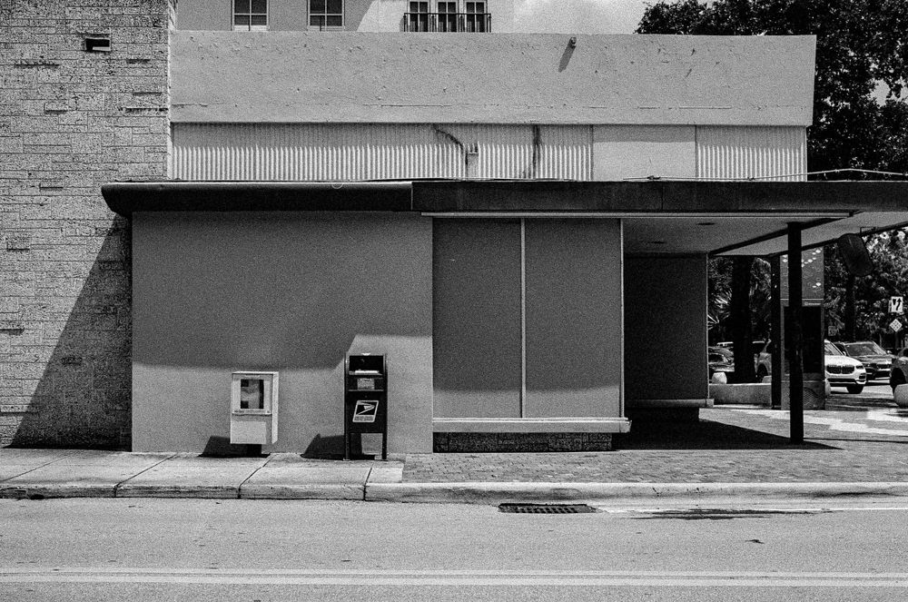 Minimalist storefront with concrete walls and a lone newspaper box on an empty street.
