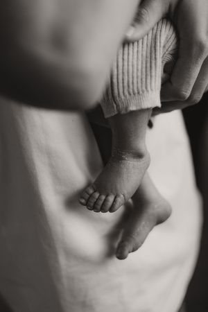 Tiny baby feet peeking out from underneath a white sweater in black and white.
