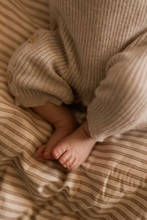Small feet resting on striped fabric with a cozy knit sweater visible.