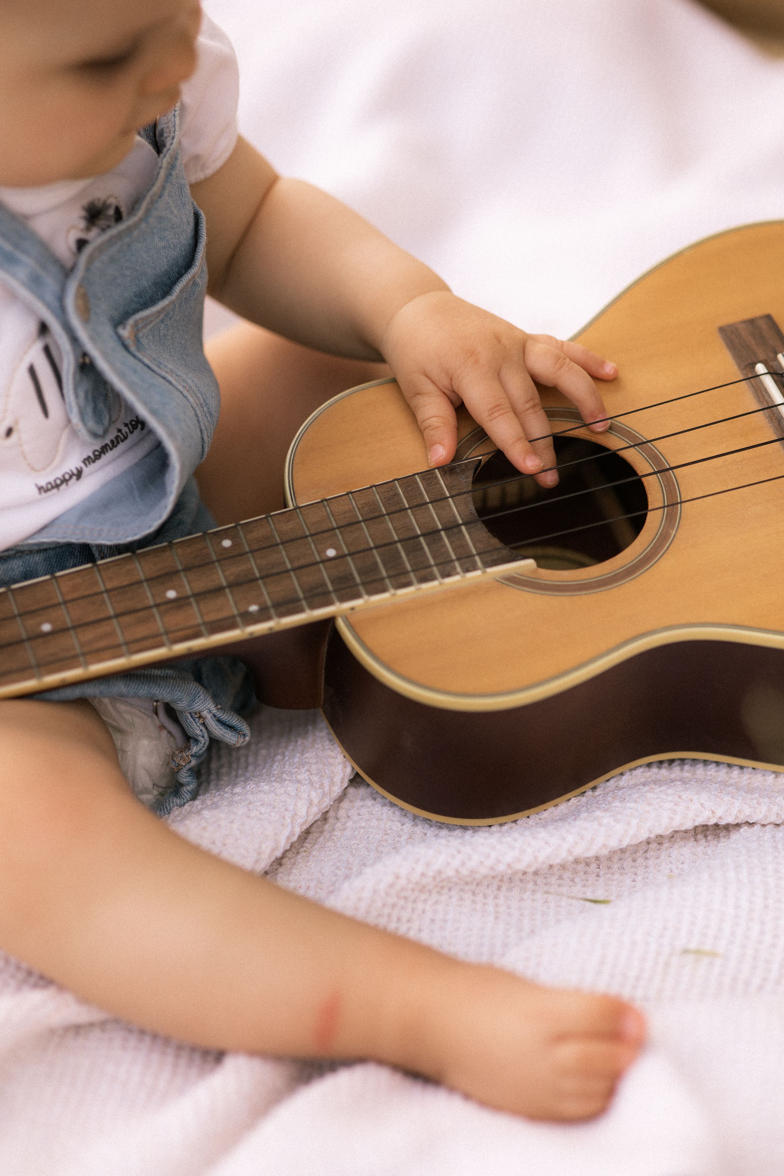 Small hands strumming strings on a wooden acoustic guitar.