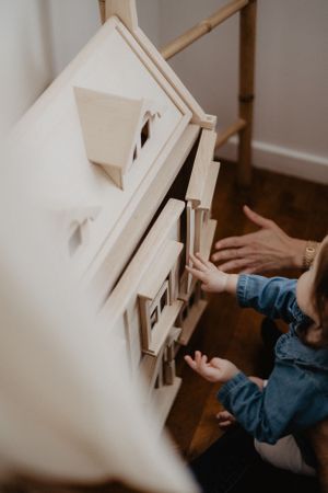 Hands interacting with a miniature white wooden dollhouse.