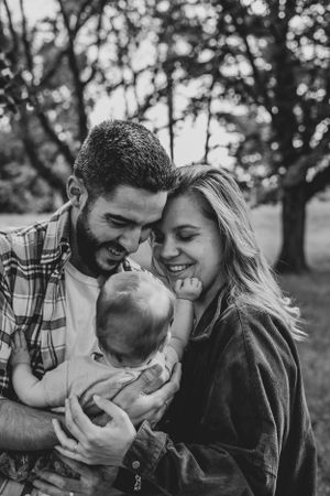 Photo en noir et blanc d'une famille. L'homme et la femme porte le bébé dans leurs bras.