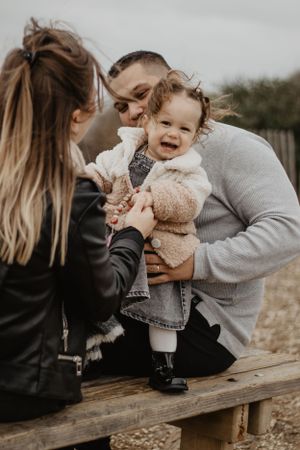 Photo d'une famille lors d'une séance. La petite fille est debout sur le banc et sa maman lui tient les mains.