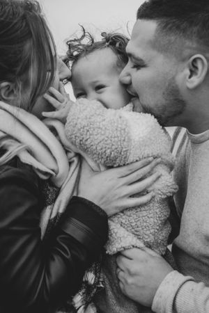 Photo en noir et blanc d'un homme, d'une femme, et de leur enfant lors d'une séance famille en extérieur.