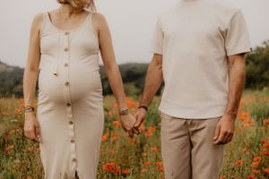 Photo d'une femme et d'un homme se tenant la main dans un champ de coquelicot. La femme est enceinte