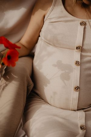 Photo du ventre d'une femme enceinte lors d'une séance grossesse. Elle tient un coquelicot qui crée une ombre