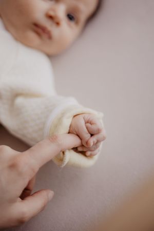 Photo d'un bébé qui tient le doigts de sa mère.