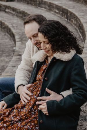 Photo d'un couple pour une séance grossesse. L'homme enlace la femme et poses ses mains sur son ventre.