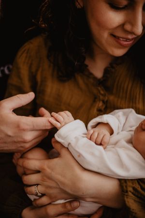 Séance photo naissance. Une maman tient son bébé, et le papa attrape la main de son bébé.