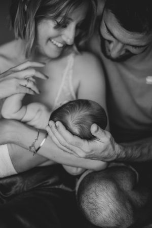 Photo en noir et blanc d'un couple tenant leur nouveau-né dans les bras. Lors d'une séance photo naissance.