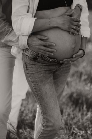 Intimate black and white photo showing hands tenderly cradling pregnant belly.