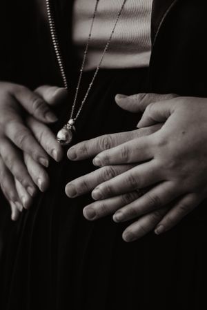 Photo en noir et blanc du ventre d'une femme enceinte. Le futur papa et la maman ont leurs mains sur le ventre