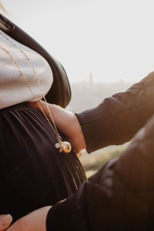 Photo d'un ventre de femme enceinte lors d'une séance grossesse. Le futur papa pose ses mains sur le ventre