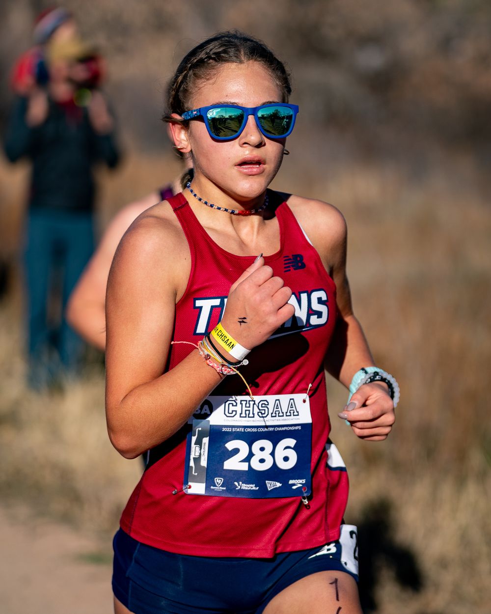 Cross country runner in red uniform competing in sunny conditions wearing blue sunglasses.