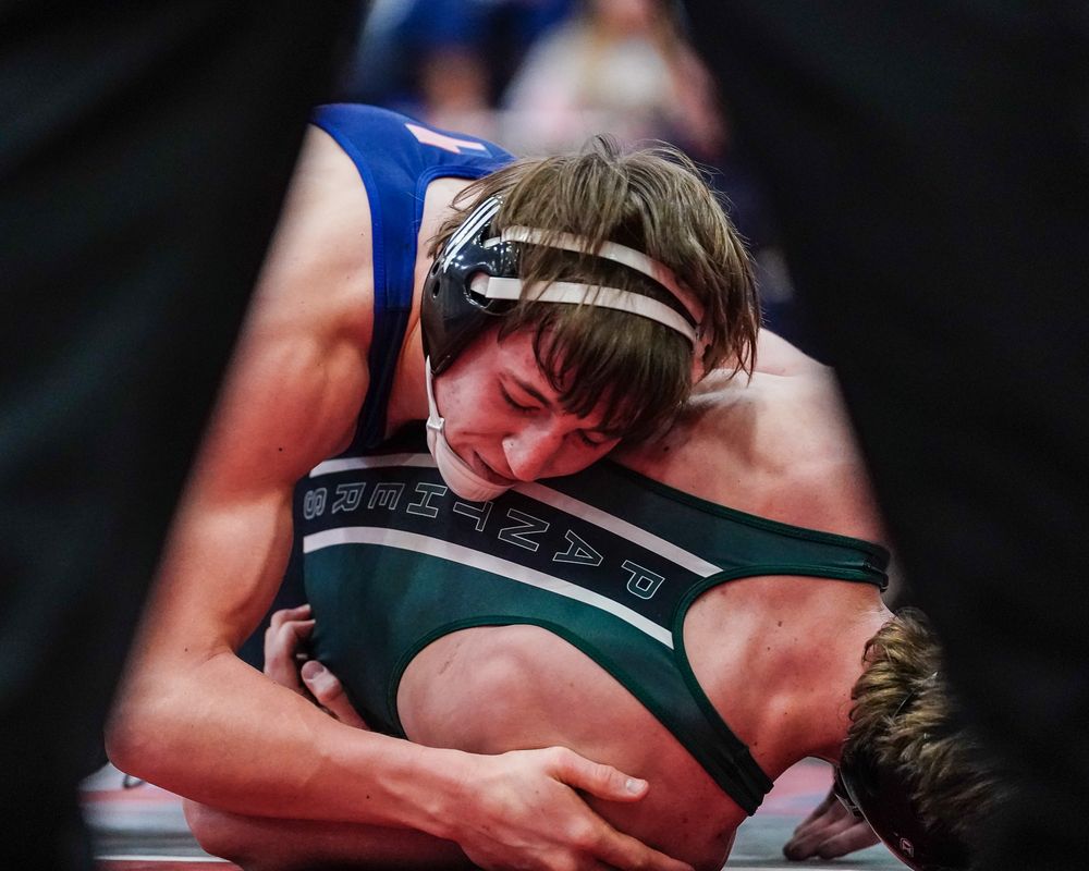 Two wrestlers competing intensely on the mat during a high school match.