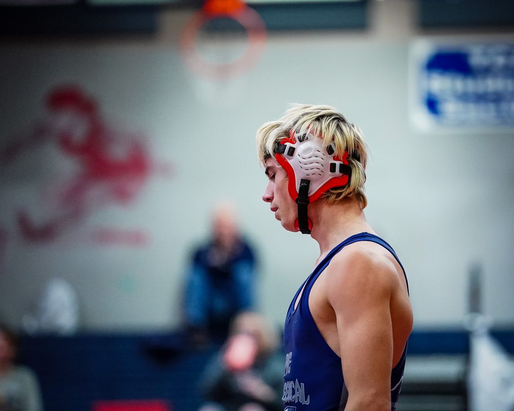 Wrestler in blue singlet wearing protective headgear during a match.