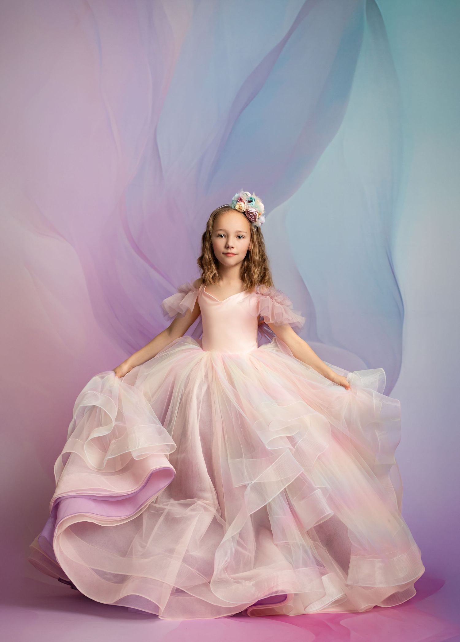 A young dancer in a flowing pink princess ball gown poses gracefully against a dreamy purple and blue backdrop.