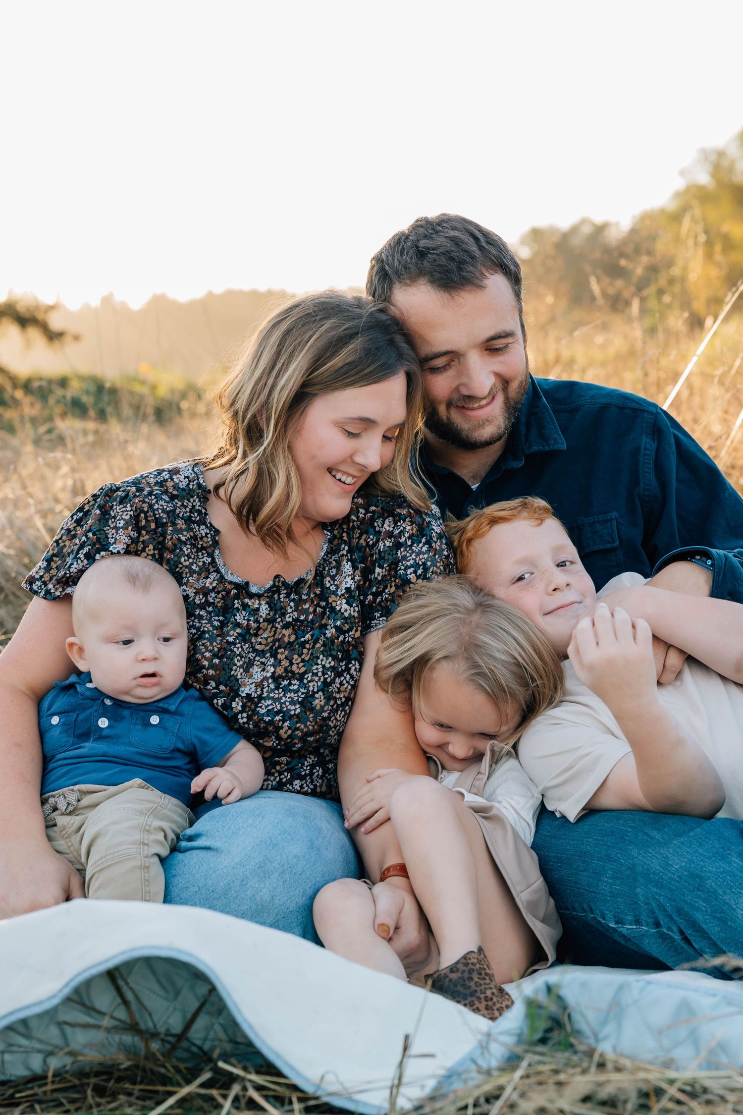 Happy family of five sitting together on a blanket in a sunlit autumn field.
