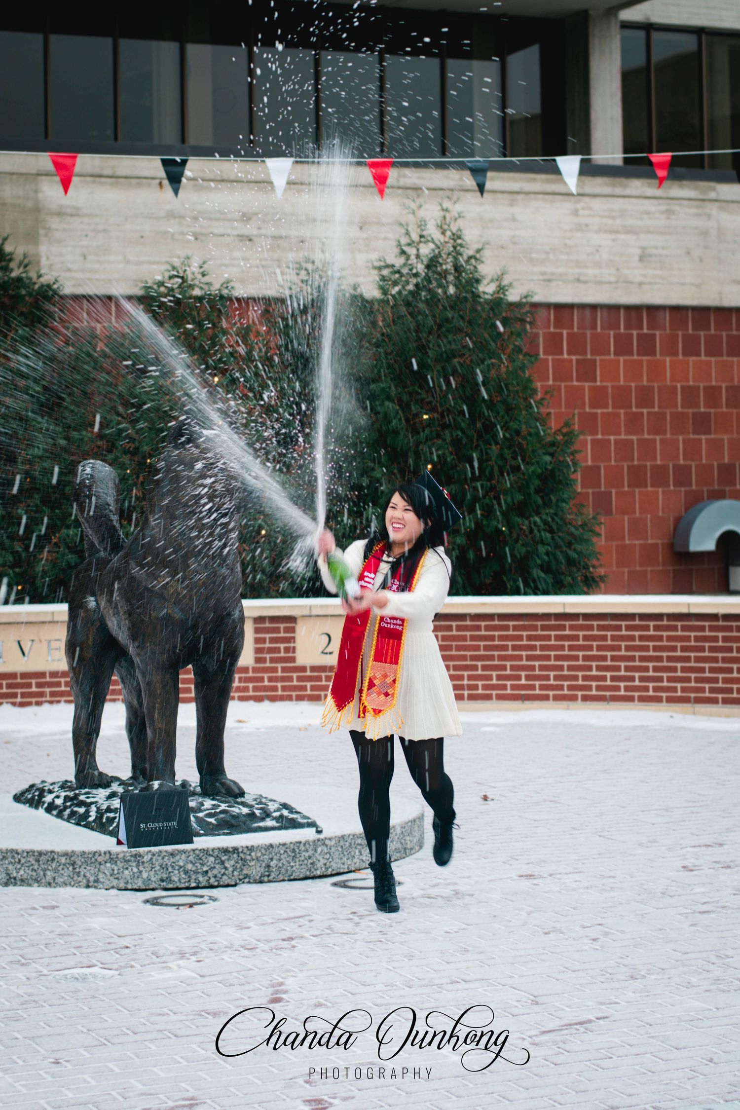 A playful winter graduation photo with spraying champange near a husky statue.
