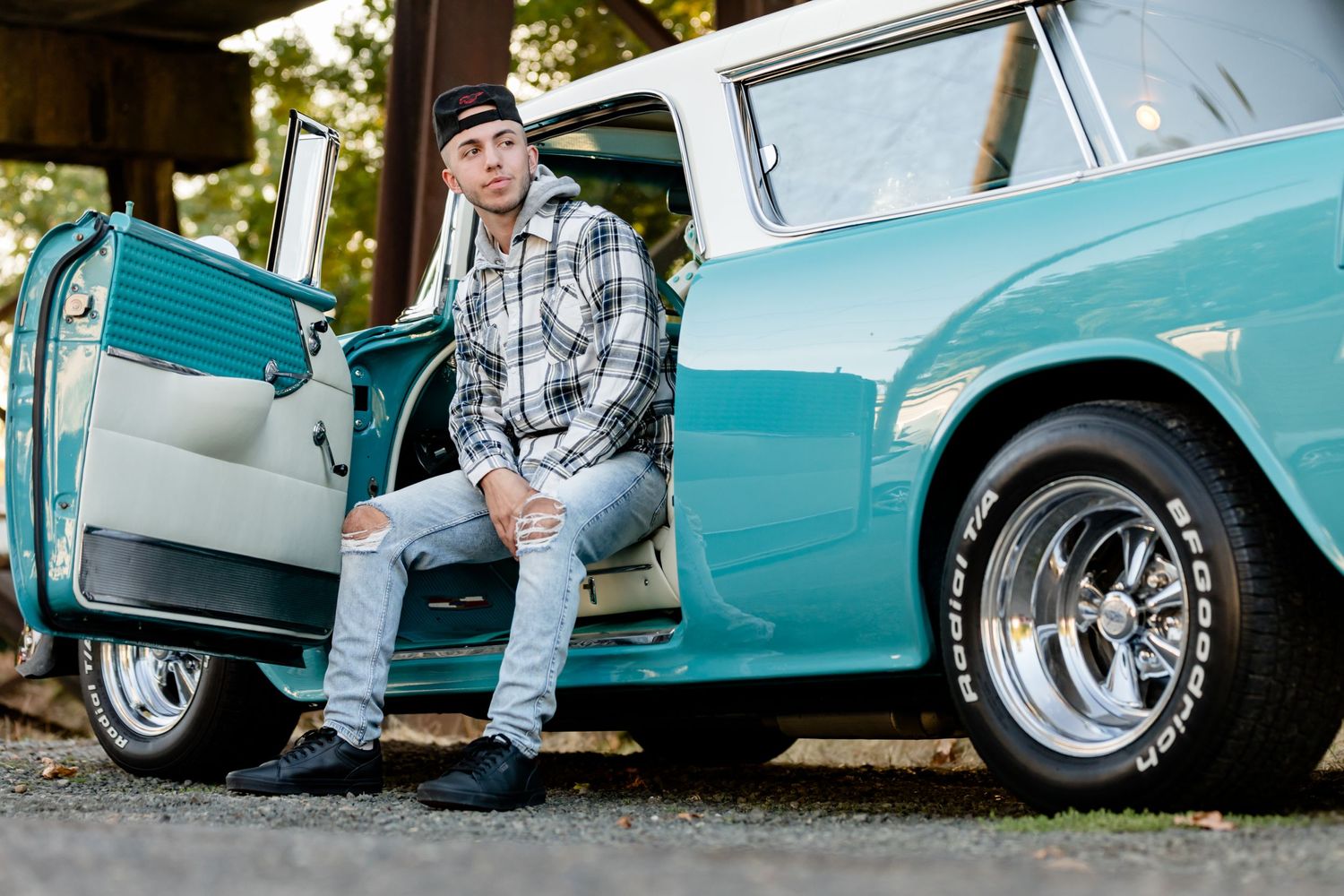 Classic turquoise vintage car with chrome wheels and open door sitting in outdoor setting.