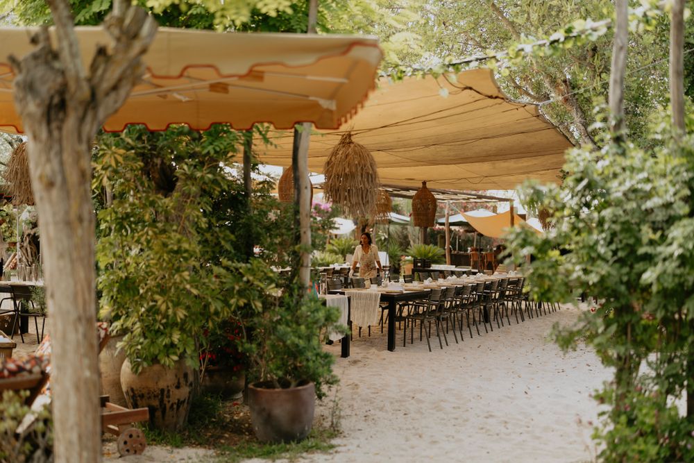 A beautiful outdoor restaurant patio with wooden awnings and hanging lanterns surrounded by lush greenery.