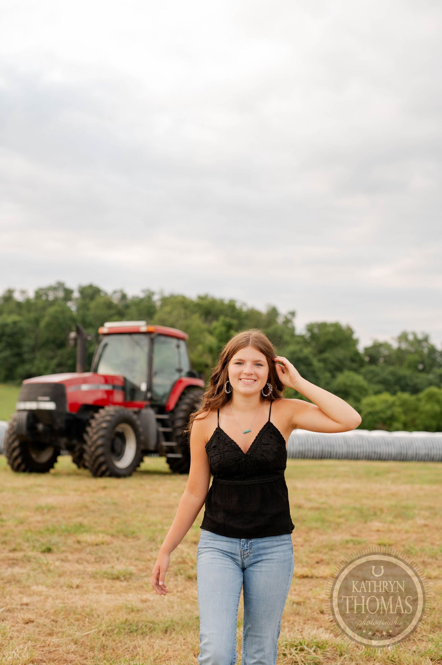 A casual outdoor portrait in front of a red tractor with fields and trees in background.