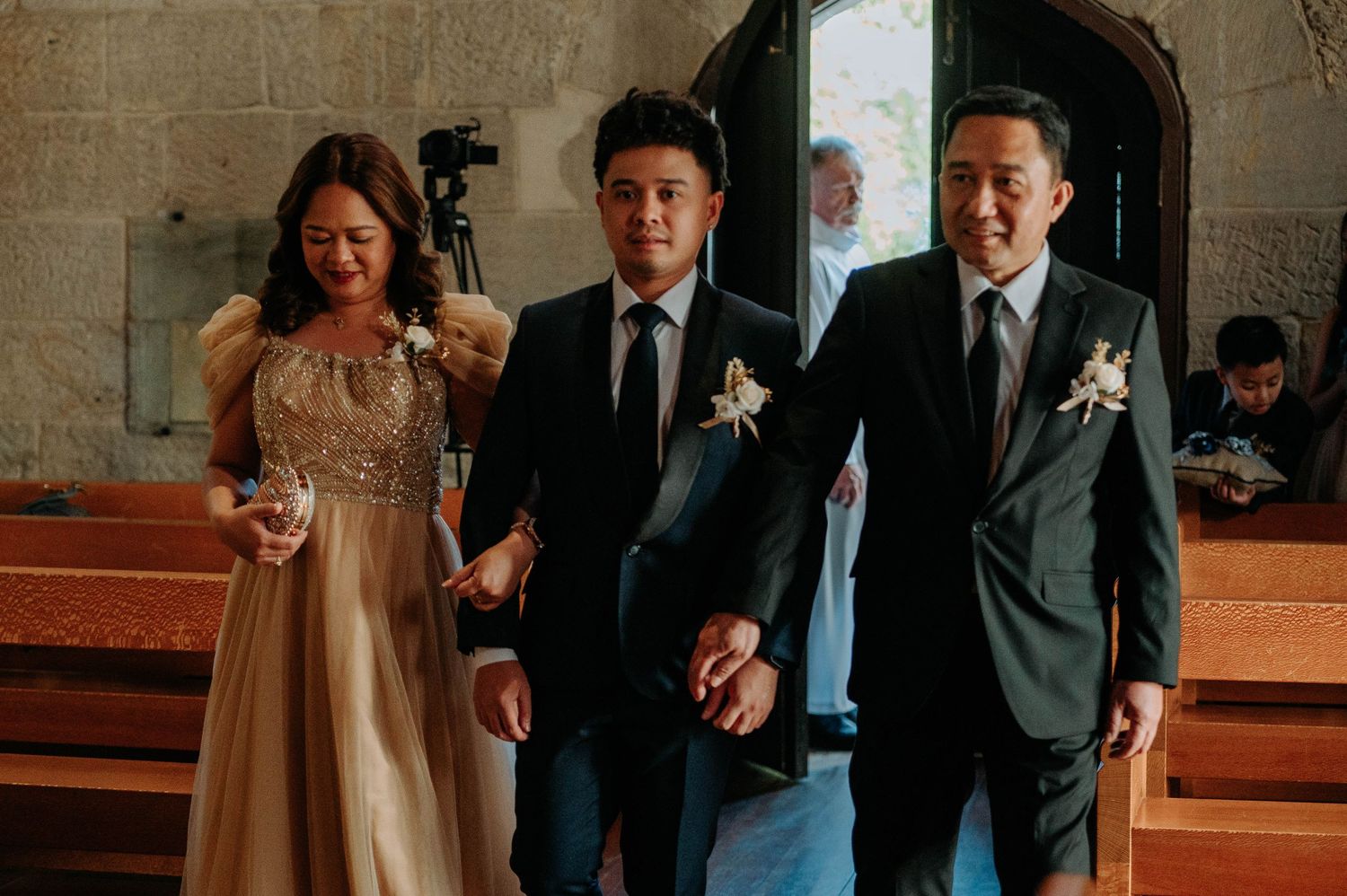 Wedding party members walking down church aisle in formal attire.