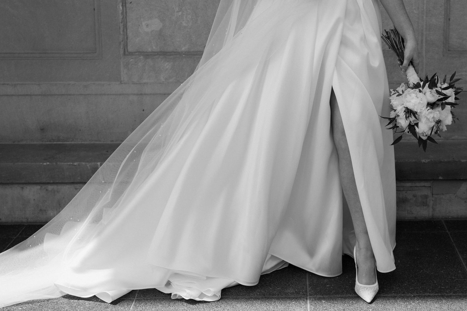Classic black and white photo showing embrace of couple in wedding attire.