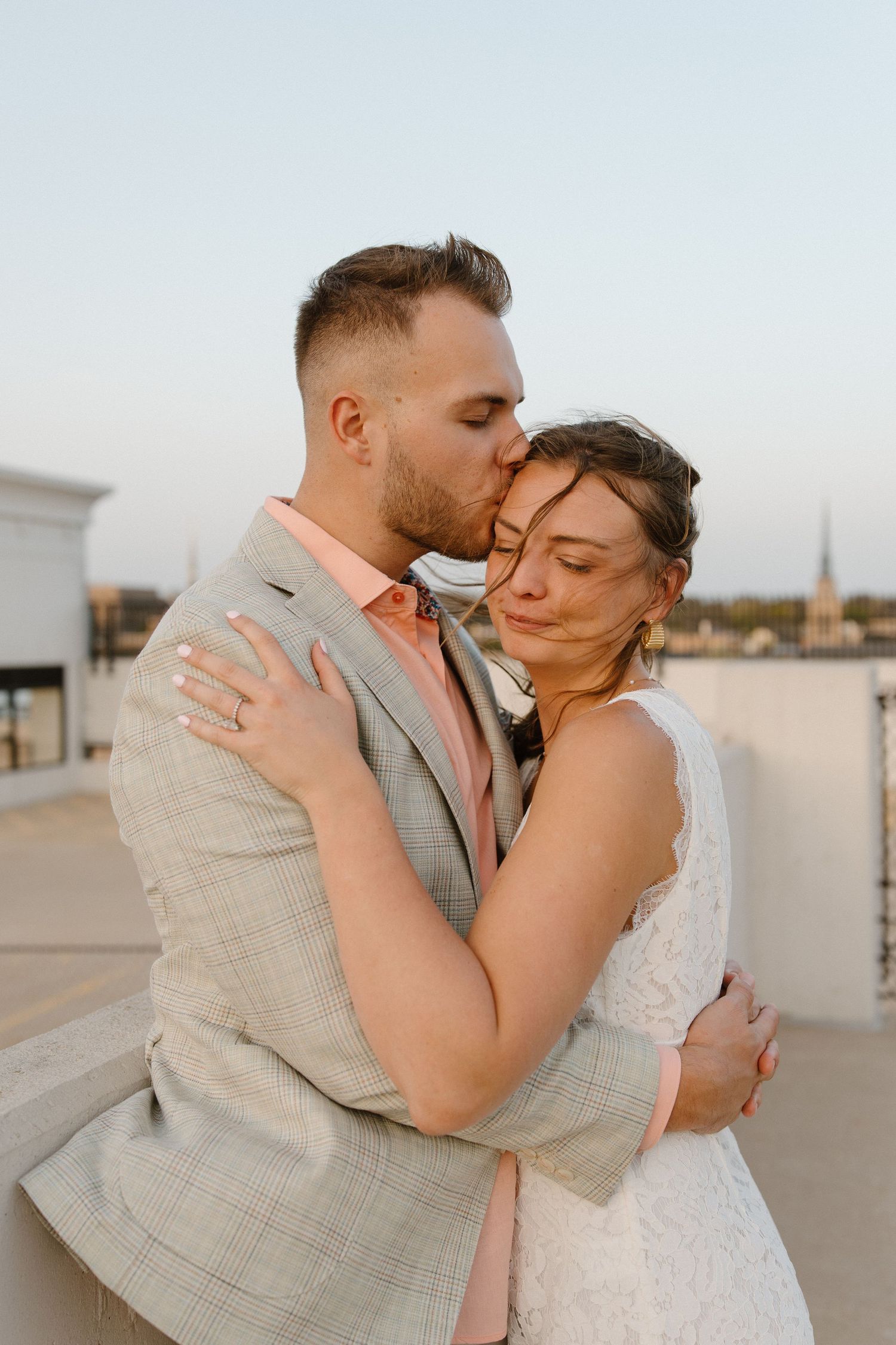 A couple embracing on a pier with a lighthouse and crashing waves in the background.