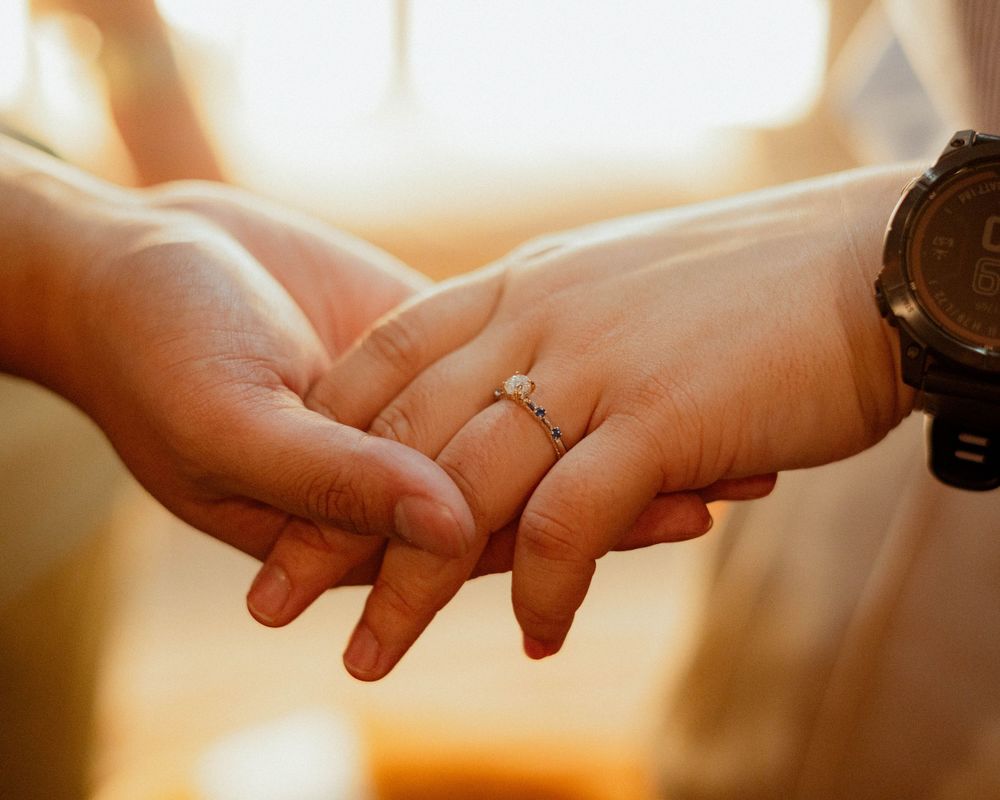 Close-up of hands holding each other, showing off new engagement ring in warm sunlight.