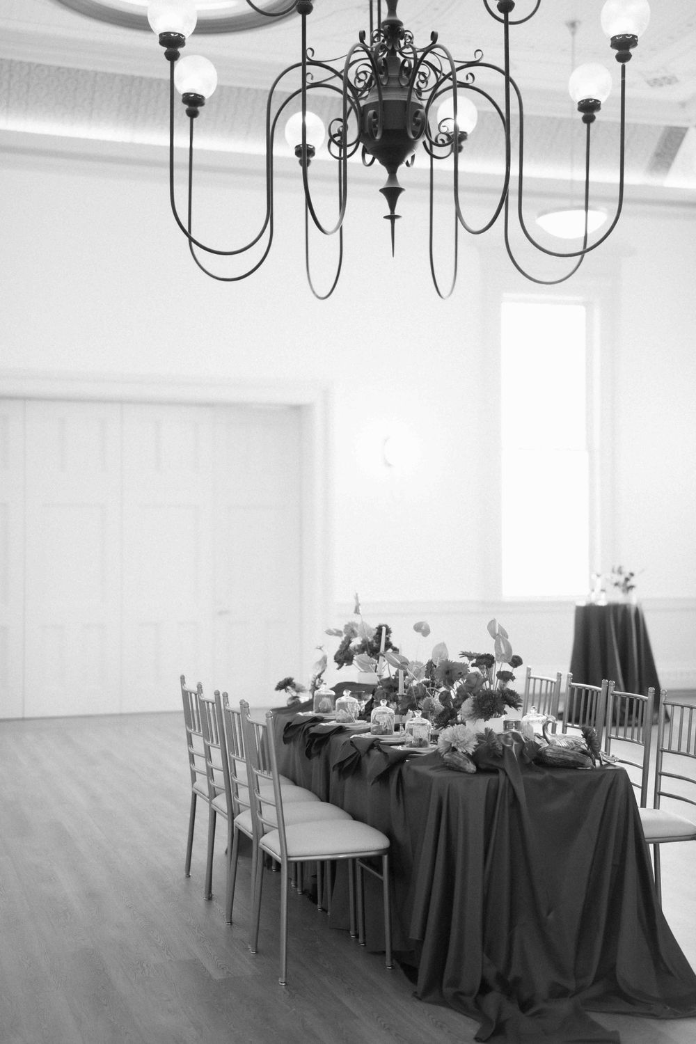 A formal dining setup under a black chandelier with a long table draped in dark linens. Location: Events at Ethereal Courthouse Square.