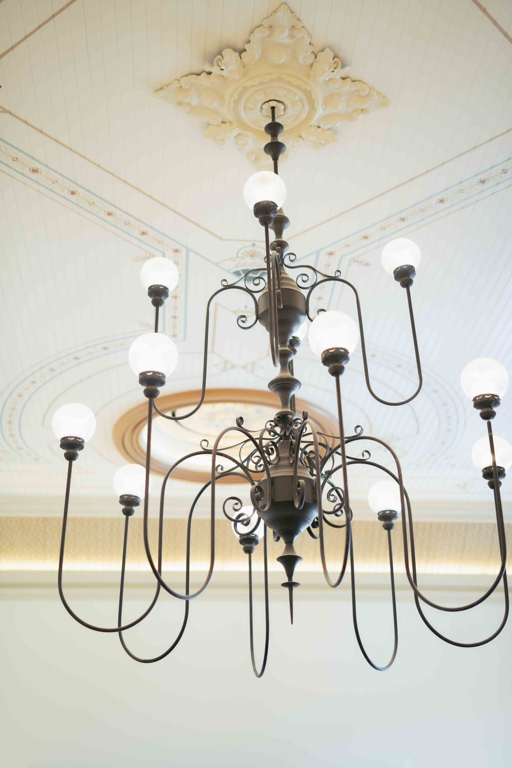 An ornate vintage chandelier with curved metal arms hangs from a decorative ceiling medallion. Location: Events at Ethereal.