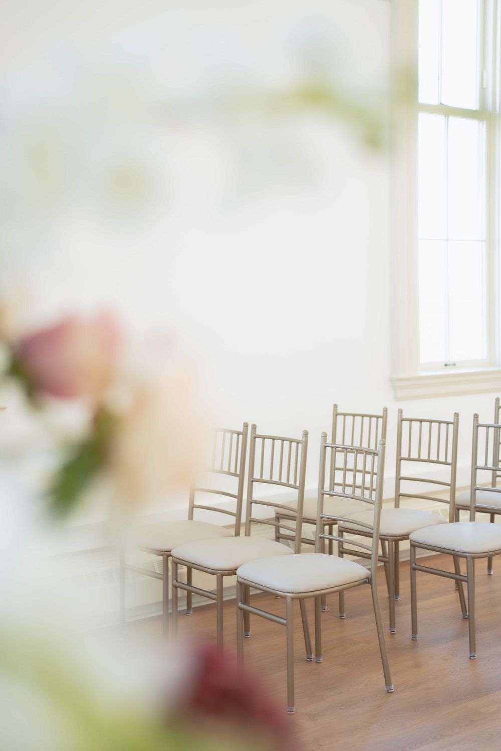 Soft focus view of chiavari chairs in a bright ceremony space with floral decor. Location: Courthouse Square Events at Ethereal.