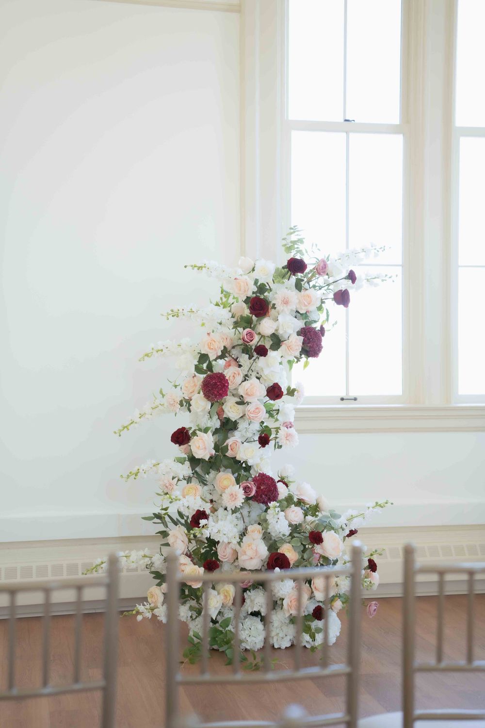 Romantic floral arrangement with white and burgundy blooms cascading upward beside a window. Location: Courthouse Square Events at Ethereal.