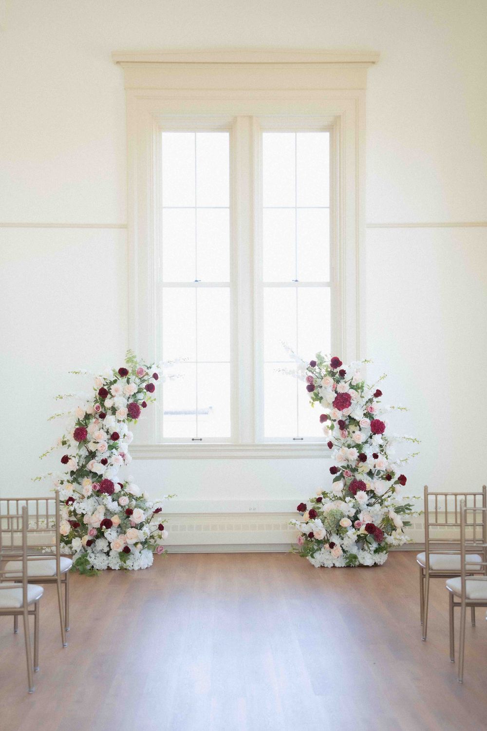 Light-filled ceremony space with climbing floral arrangements framing a tall window. Location: Courthouse Square Woodstock, IL.