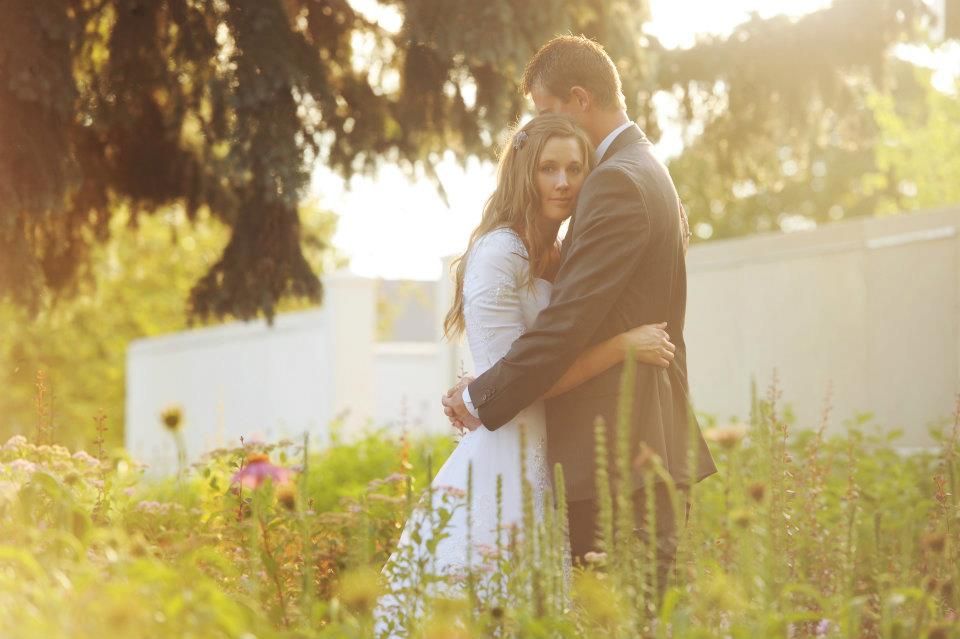 A romantic couple embraces in a sunlit meadow at golden hour surrounded by wildflowers.