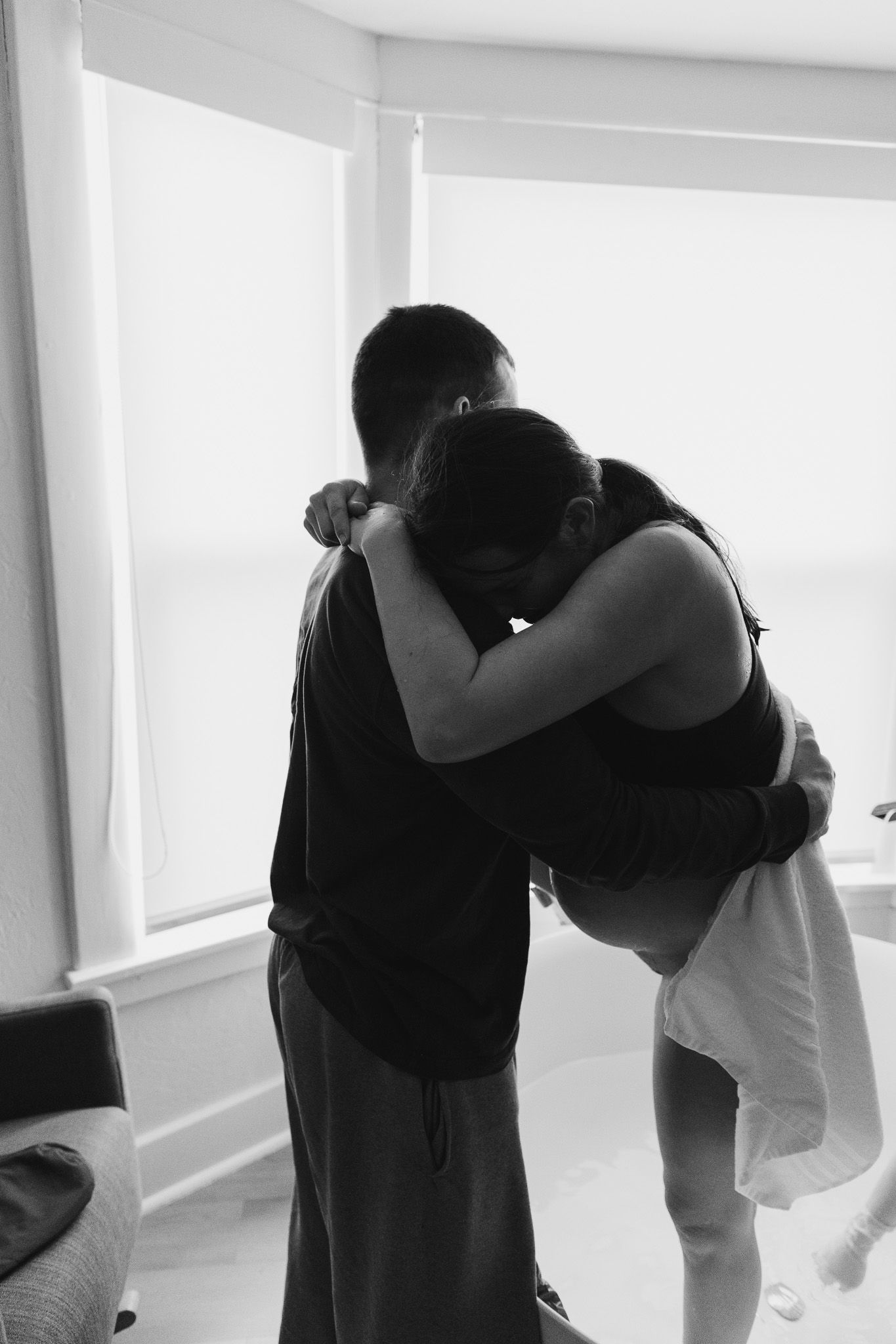Intimate black and white photo of couple embracing in bright room.