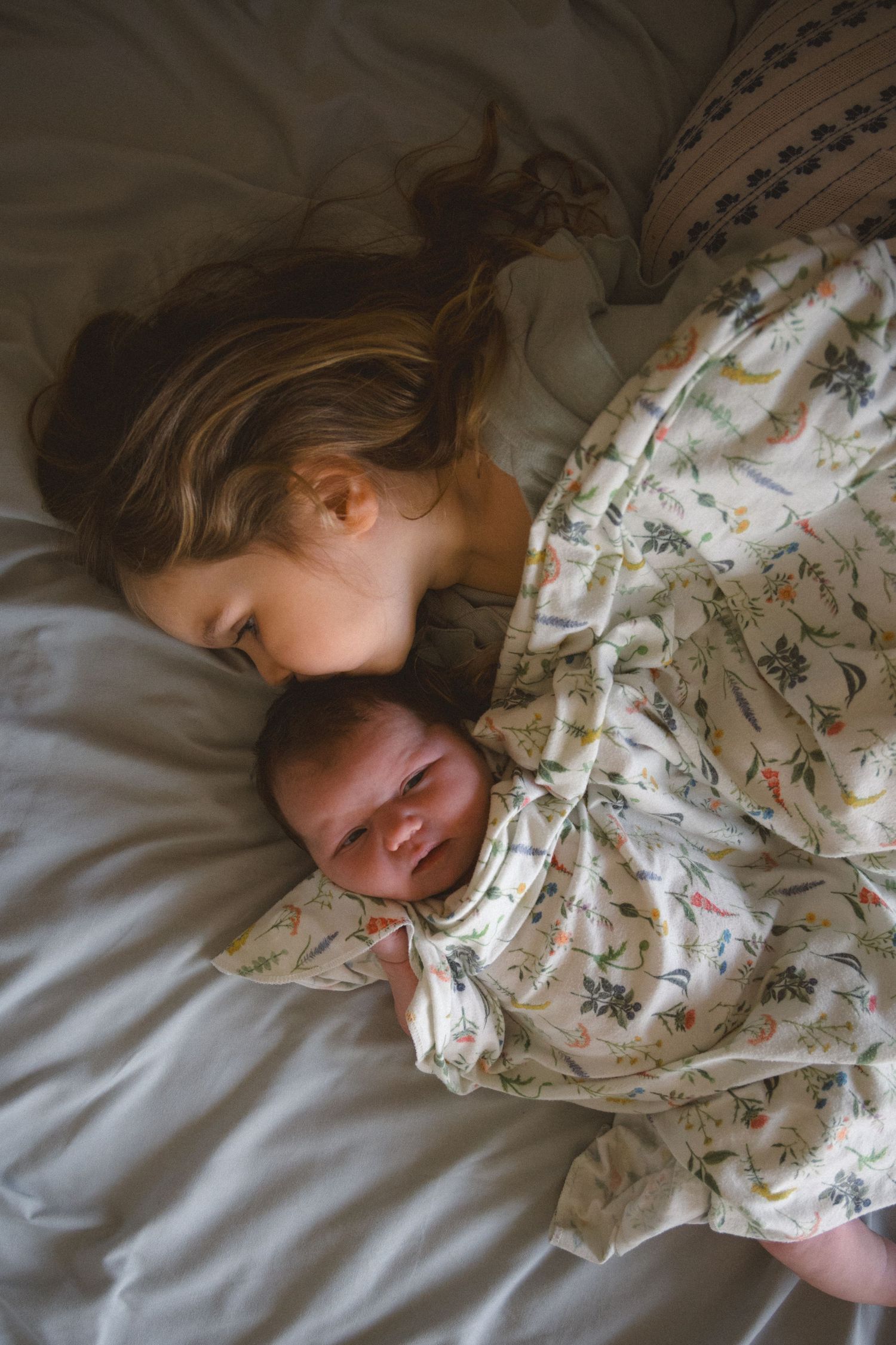 newborn and toddler sister cuddling on bed
