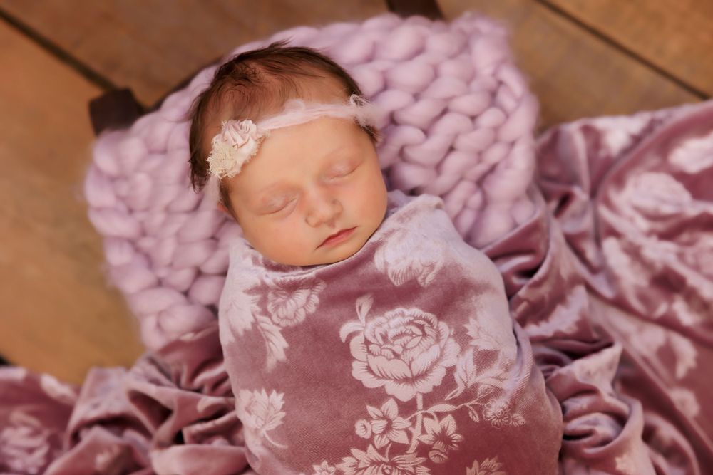 Newborn baby sleeps on pink knit blanket with floral pattern wrap.