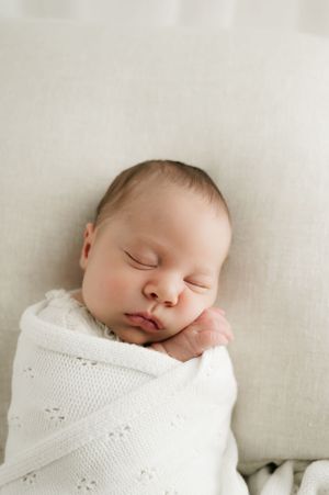 Peaceful sleeping newborn wrapped in white textured blanket against neutral background.