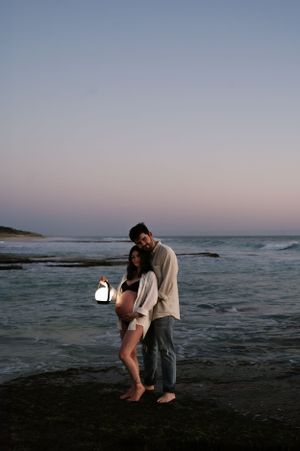 A couple embraces on a misty beach at sunset with waves crashing in the background.