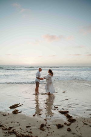 A romantic beach scene at sunset with a couple standing in the gentle surf, creating a dreamy atmosphere.