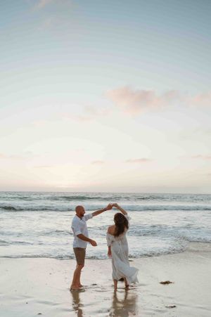 Couple dancing together on a serene beach during sunset with gentle waves rolling in the background.