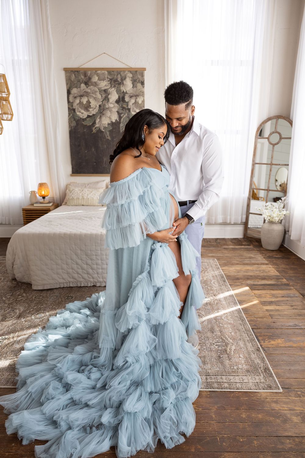 A couple shares an intimate moment in a bedroom, with the woman wearing a flowing light blue ruffled gown.