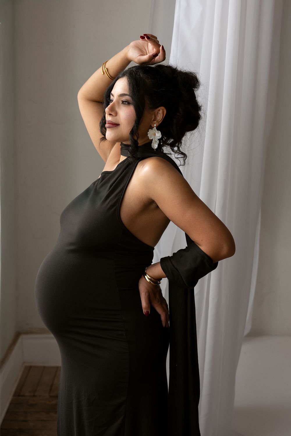 A person in a black sleeveless dress poses expressively against white curtains in a series of artistic movements.