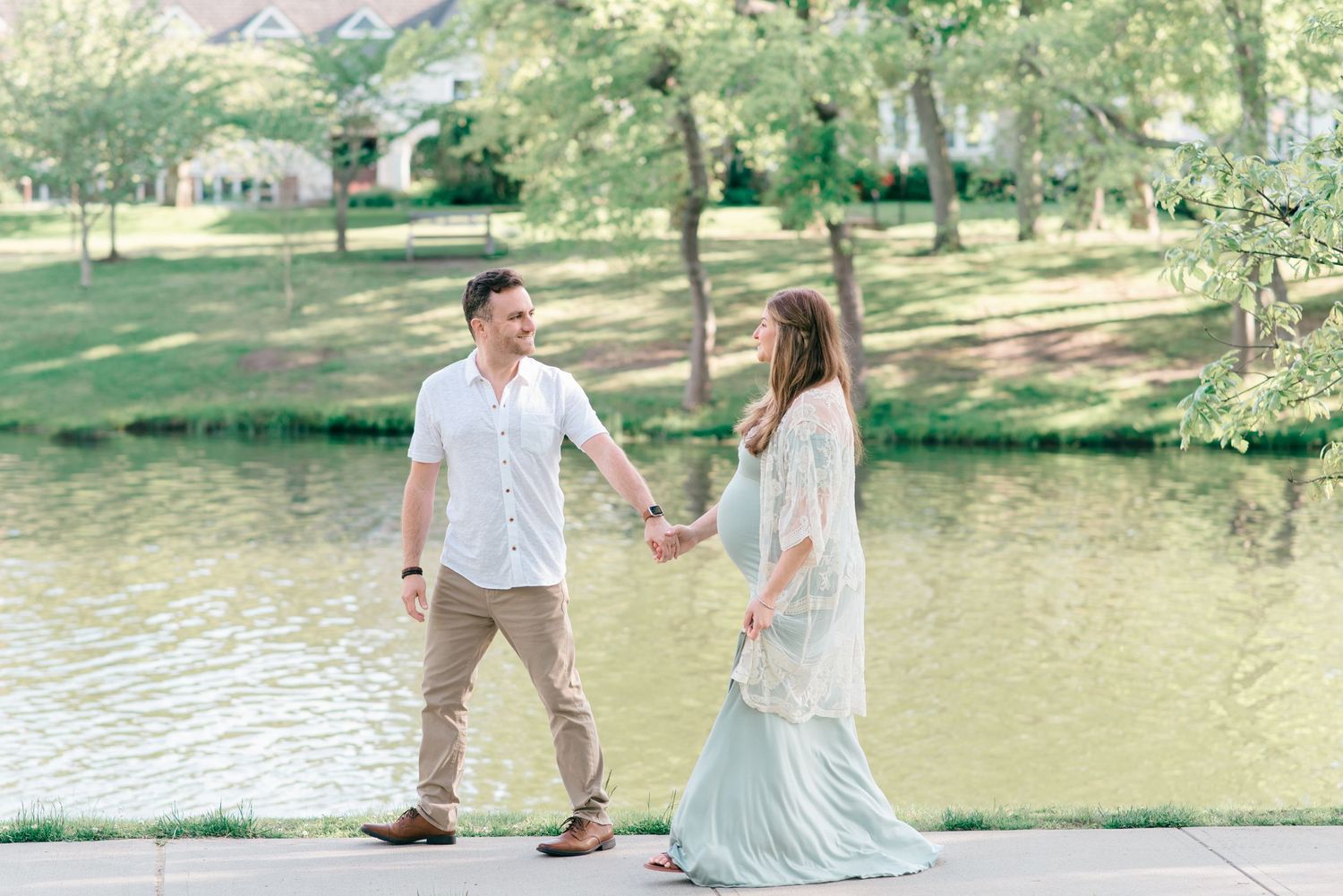 A young couple walk in front of a lake looking into each other's eyes.