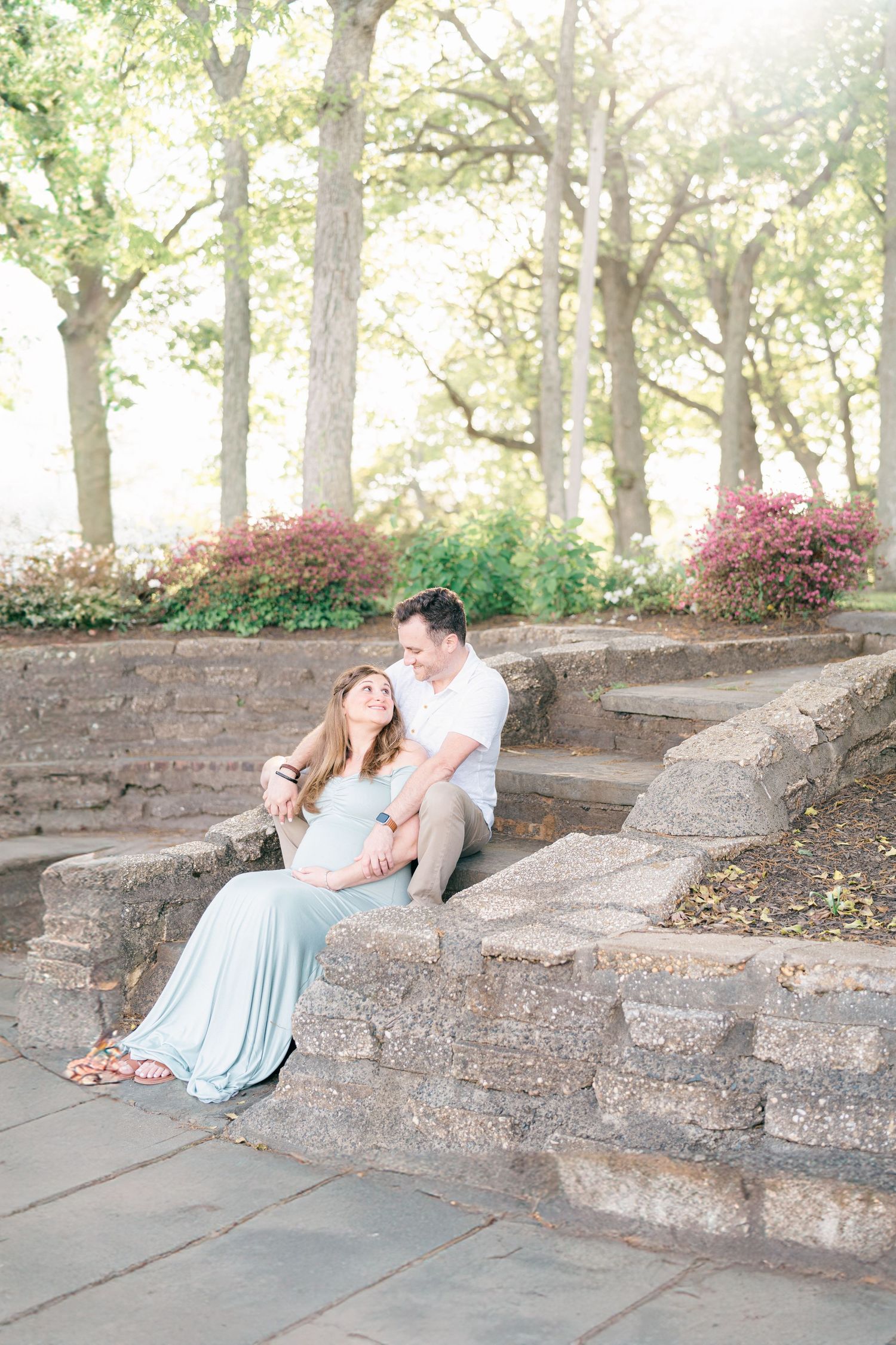 A couple pose together on stone steps in front of the lake at Divine park.