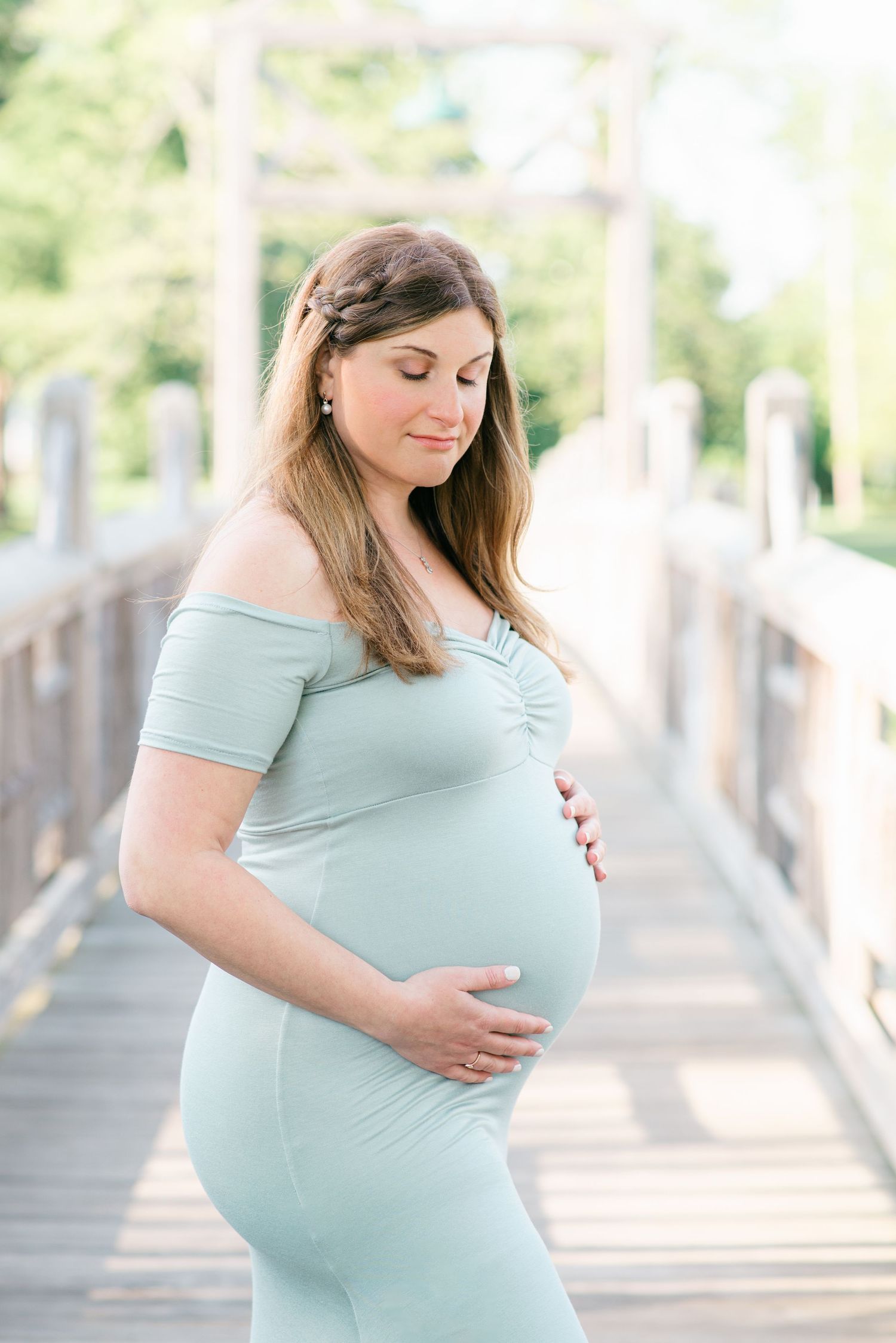 Pregnant woman poses on a bridge while holding her belly.