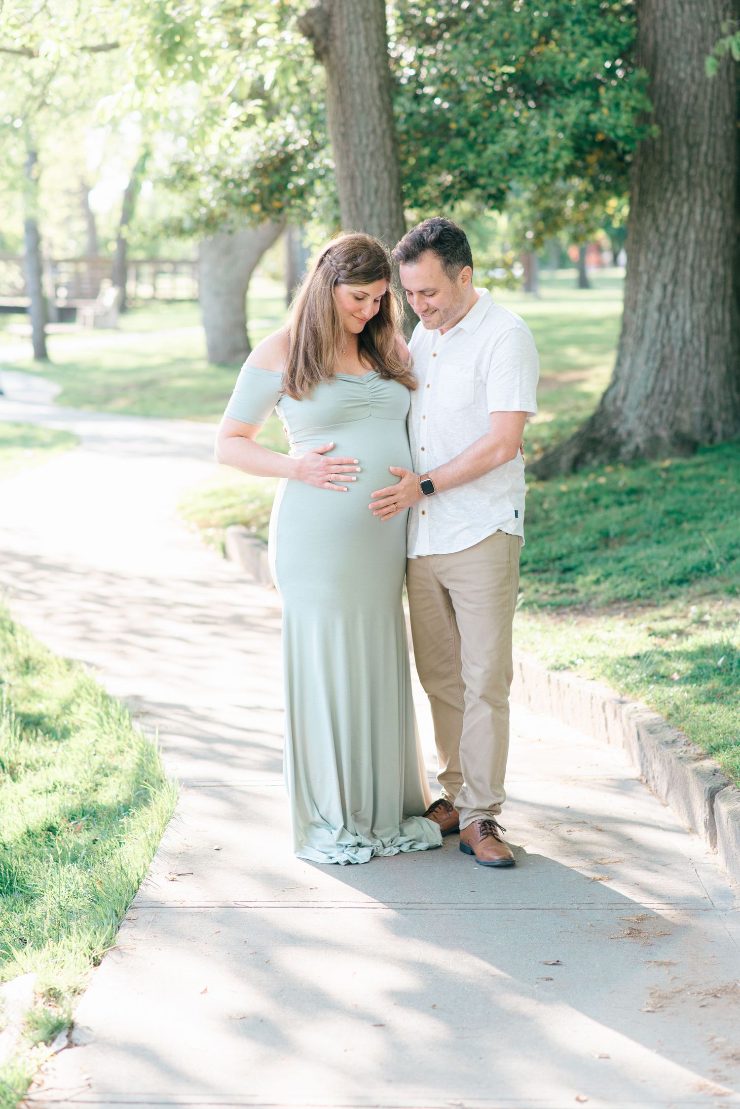 Mom-to-be and man in a beautiful maternity gown standing near a lake, the soft glow of the sunset lighting the scene in Monmouth County.